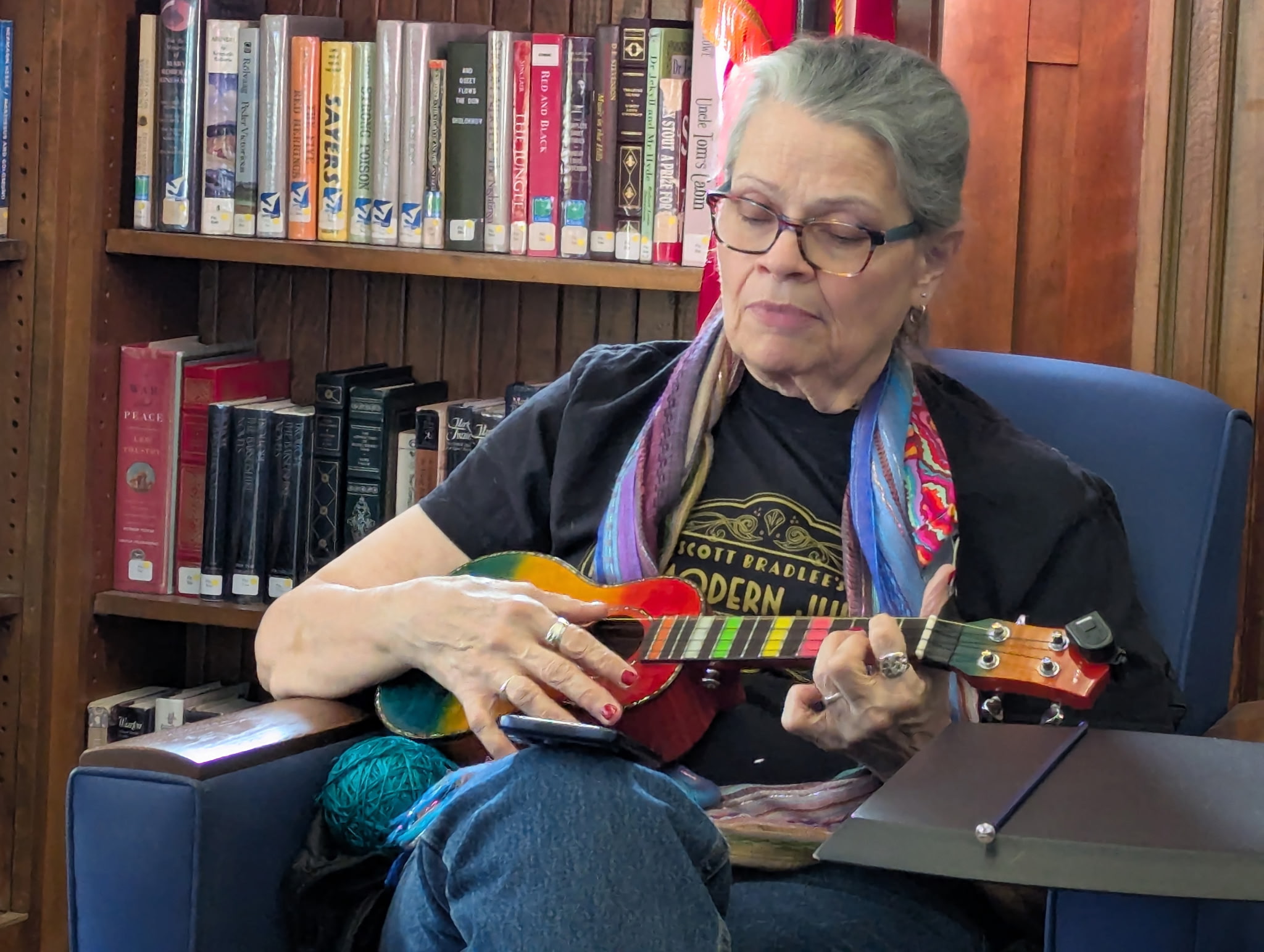Ukulele player seated among library books with a colorful ukulele