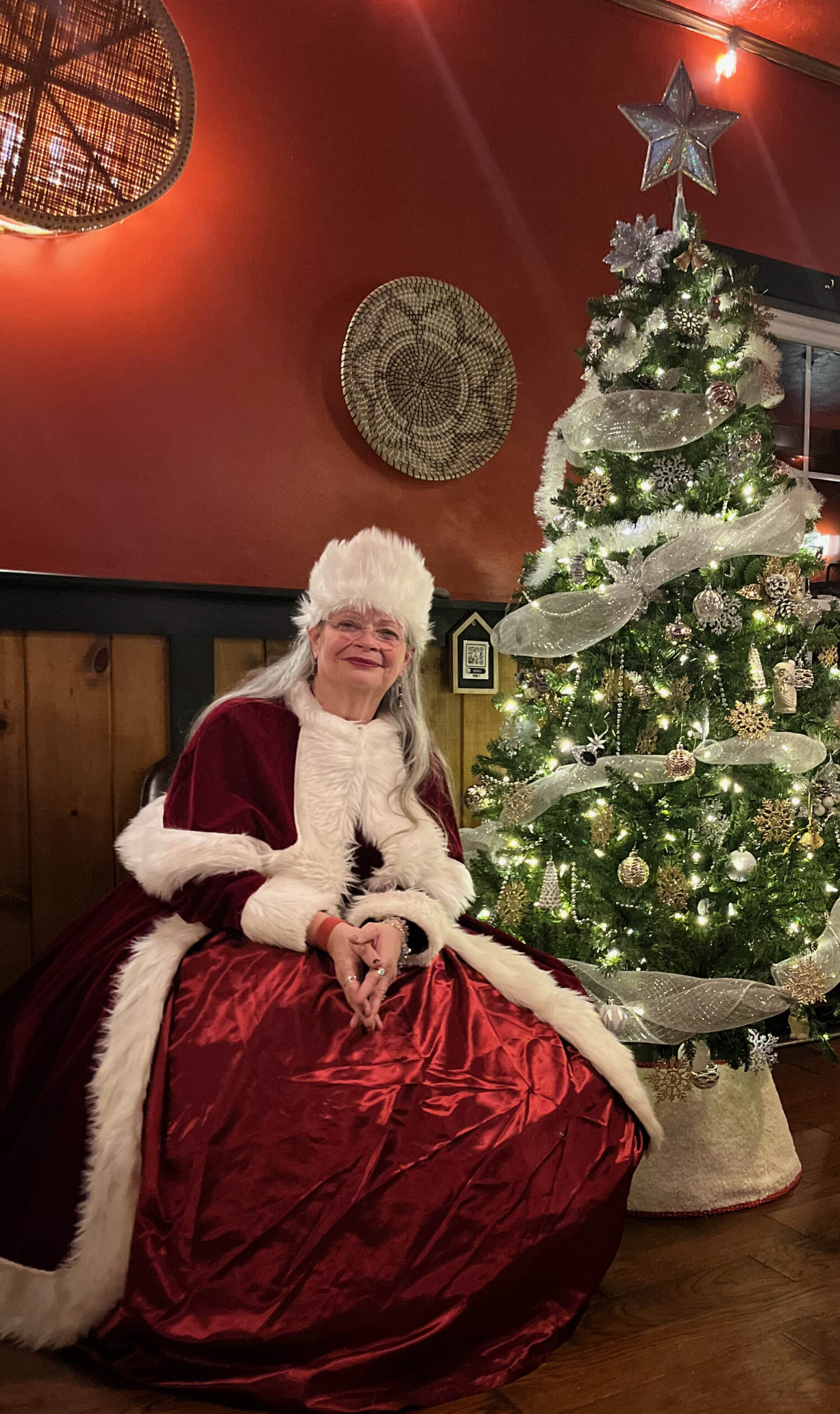 Mrs Anna Claus seated beside a decorated Christmas tree at Sturbridge
